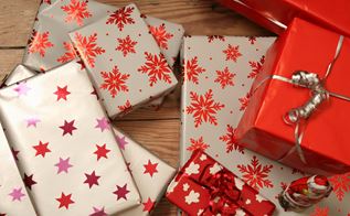 Seks julegaver i hvidt, rødt og gråt papir i en bunke på et trægulv